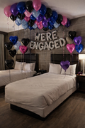 Decorated bedroom with balloons and 'WE'RE ENGAGED' sign above two beds.