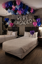Decorated bedroom with balloons and 'WE'RE ENGAGED' sign above two beds.